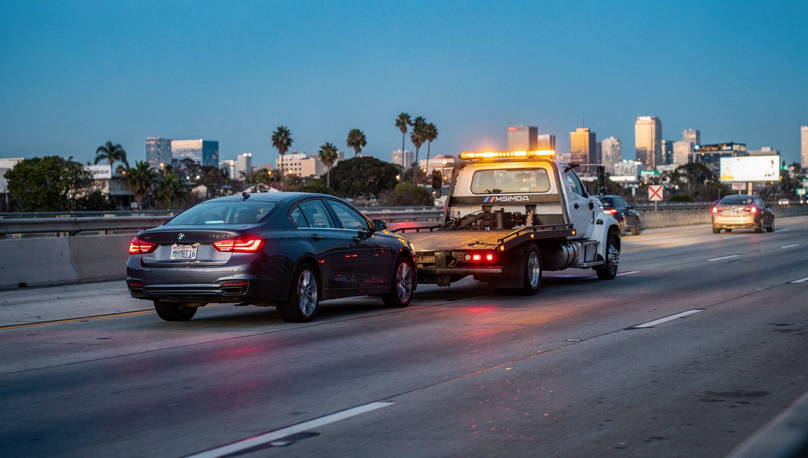 Tow truck approaching a disabled car during a San Diego freeway breakdown at dusk